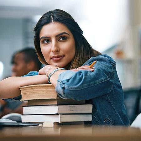 Student rests chin on hands folded over stack of books